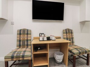 A room with a TV mounted on the wall, two plaid chairs, a small wooden table, a trash bin, and a power outlet. - Luxury Winter Gardens Apartment 1 (Blackpool)