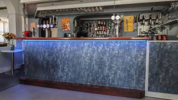 A bar area with a sign reading 'LET THE WEEKEND BE-GIN,' a selection of bottles, glasses, and a blue bar counter.
