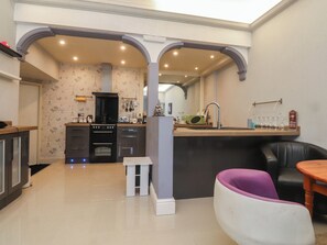 Une cuisine moderne avec un îlot central, un coin repas agrémenté d’une chaise violette et un canapé en cuir noir.