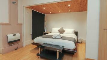 A bedroom with a bed, bedside tables, a wooden ceiling, and a wall-mounted hand dryer.
