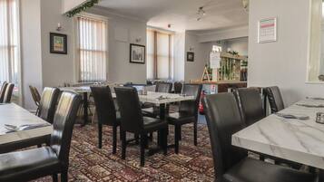 A dining area with tables and chairs, a patterned carpet, and framed pictures on the walls.