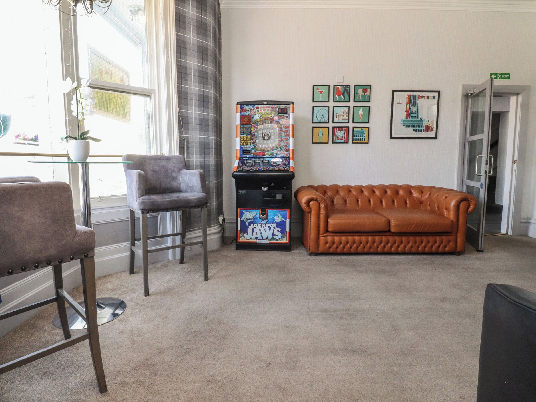 A room with a brown leather sofa, a grey armchair, a small table with a potted plant, and a slot machine.