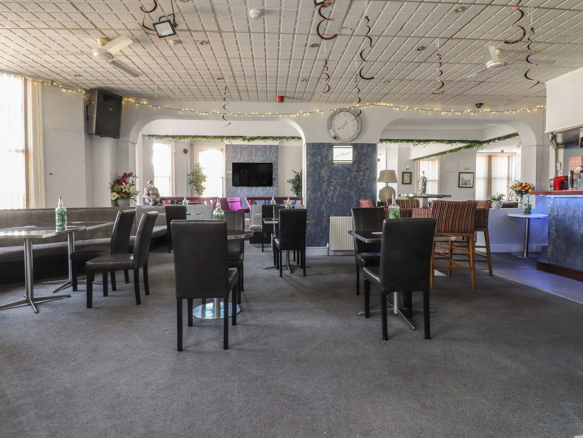A spacious room with a dining area, a bar, and a television mounted on the wall.