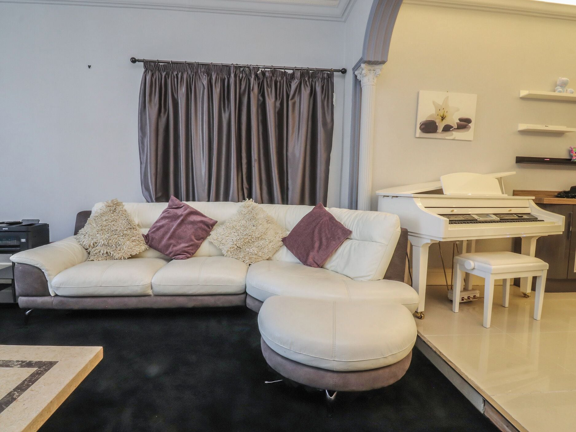A living room with a white sofa, a piano, and a small table.