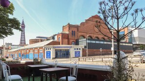 Outdoor seating with tables and chairs, a brick building with a sign, and a tower in the background. - Luxury Winter Gardens Apartment 2 (Blackpool)