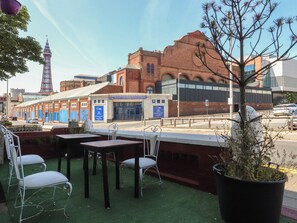 Outdoor seating with tables and chairs, a brick building with a sign, and a tower in the background. - Luxury Winter Gardens Apartment 2 (Blackpool)