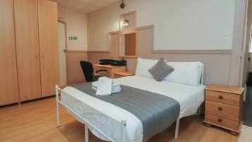A hotel room with a bed, bedside table, wardrobe, desk, chair, and a mirror.