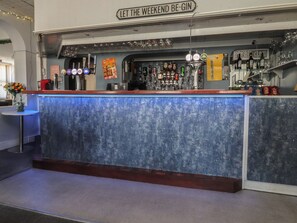Un espace bar agrémenté d’une enseigne sur laquelle on peut lire : « QUE LE WEEK-END COMMENCE ! », ainsi qu’un assortiment de bouteilles, de verres et un comptoir de bar bleu.