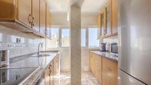 A modern kitchen with granite countertops, stainless steel appliances, wooden cabinets, and a central marble column. - Almería Suite: Cathedral Penthouse (Almería)