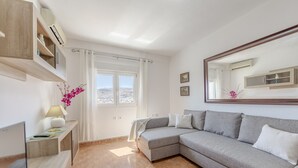 A modern living room with a grey sofa, a TV, a lamp, and a window with curtains. - Almería Suite: Cathedral Penthouse (Almería)