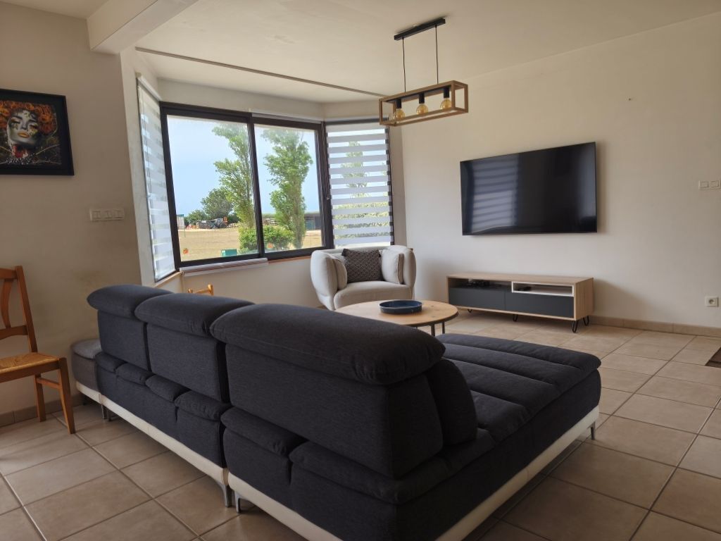 A modern living room with a sectional sofa, a chair, a TV, and a window with blinds.