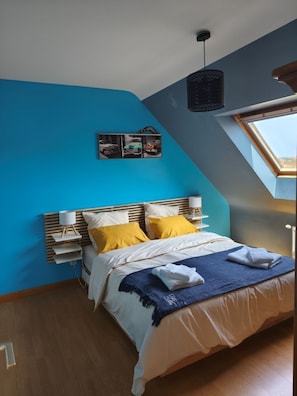 Et soveværelse med skråvæg, ovenlys, seng med hvidt og gult sengetøj samt et natbord med en lampe.