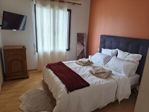 A bedroom with a bed, a television, a wooden cabinet, and a window with curtains. - House a 5-minute walk from the ocean (Plougoulm)