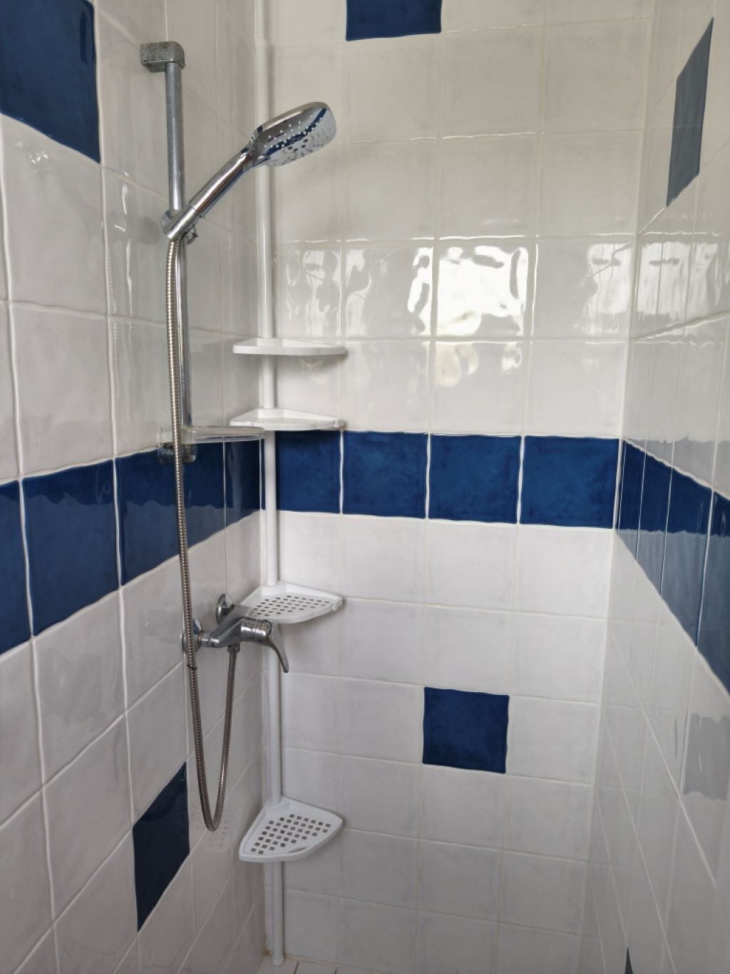 A shower area with a handheld showerhead, a wall-mounted faucet, and a handheld showerhead.