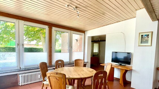 A dining area with a round wooden table and chairs, a television, and a whiteboard.