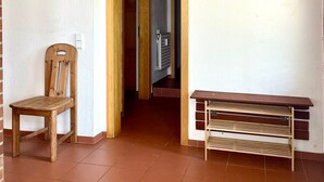 A room with a wooden chair, a bench, a picture on the wall, and a door leading to another room.