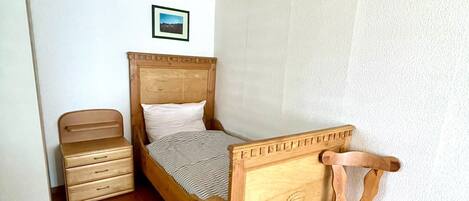 Une chambre avec un lit en bois, une table de chevet en bois, une chaise et un tableau au mur.