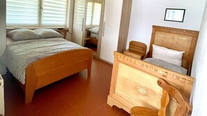 A bedroom with a wooden bed, a wooden dresser, a chair, and a window with blinds.