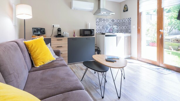 Ett modernt vardagsrum med en soffa, ett litet bord och en köksdel med mikrovågsugn och kaffemaskin.