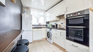 A compact kitchen with a washing machine, a microwave, a toaster, and a built-in oven. - Bright 1BR Flat w/ Free Parking & Easy City Access (Dublin)