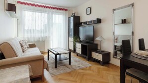 Ein Wohnzimmer mit einer Couch, einem Couchtisch, einem Fernseher, einer Lampe, einem Spiegel und einem Esstisch mit Stühlen.