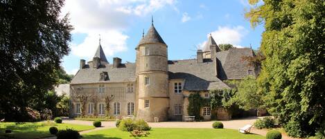 A large, historic building with multiple towers and a well-maintained garden.