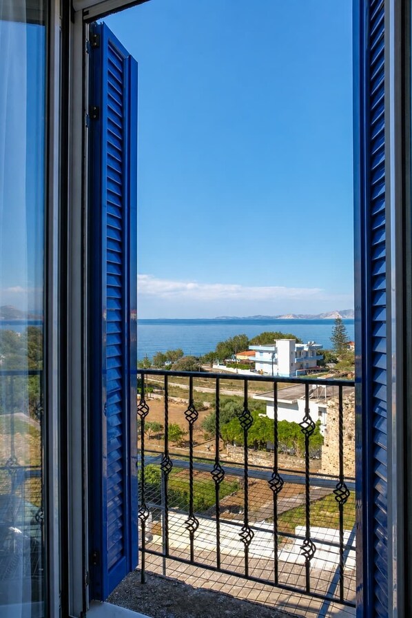 A balcony with a metal railing and a view of the sea and buildings in the distance.