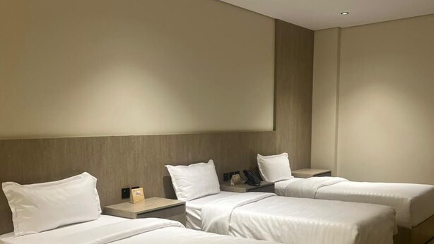 Habitación de hotel con tres camas, cabecera de madera, televisor de pantalla plana y piso alfombrado.