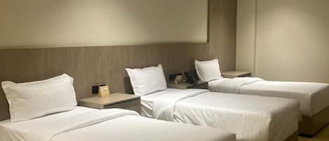 A hotel room with three beds, a wooden headboard, a flat-screen TV, and a carpeted floor.