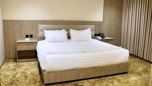Una habitación de hotel con una cama grande, una mesita de noche con lámpara y una cortina.