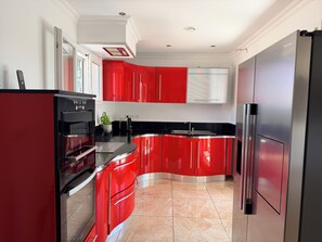 Una cocina moderna con armarios rojos, electrodomésticos de acero inoxidable y piso de baldosas.