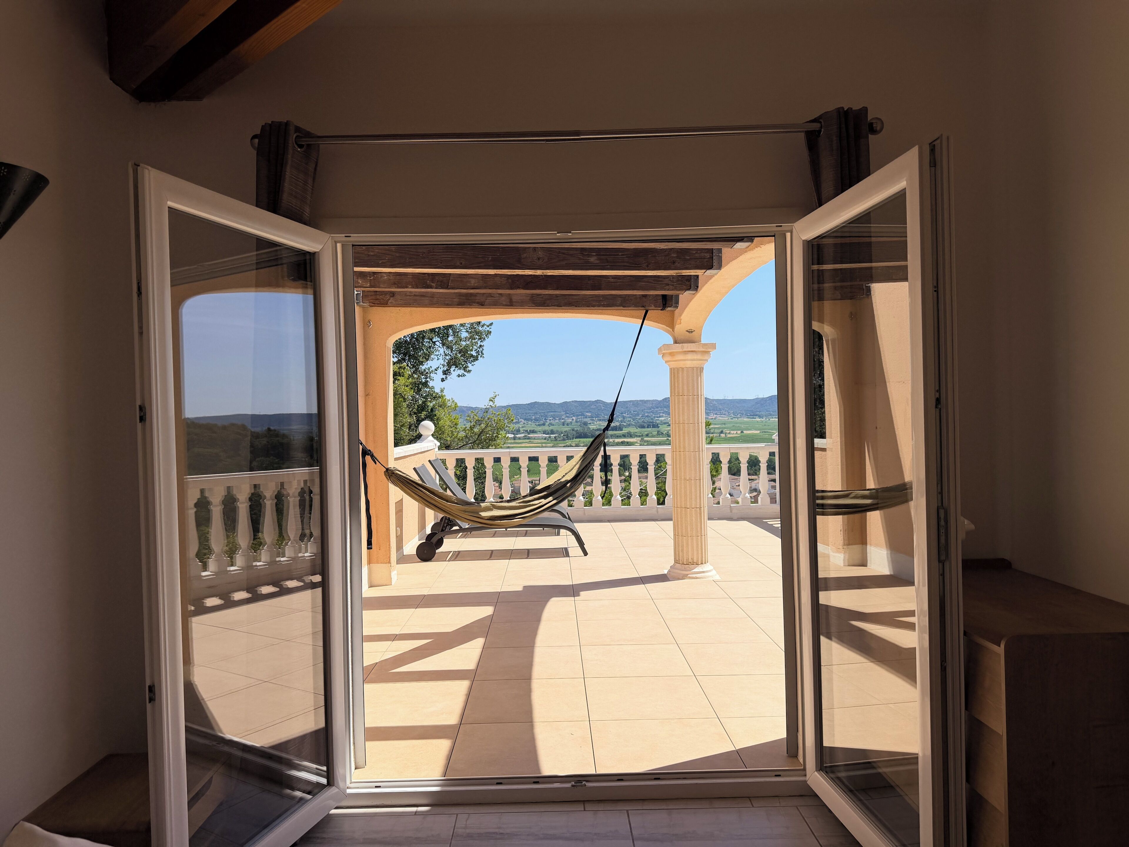 An open sliding door leading to a balcony with a hammock, a tiled floor, and a view of the landscape.