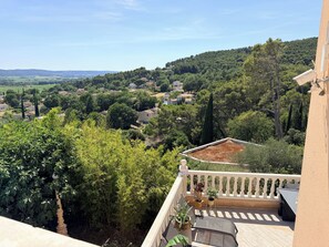 Ein Balkon mit Blick auf ein Dorf, Blumentöpfen und einer Pergola.