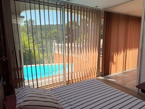 A bedroom with a view of a swimming pool and outdoor area. - Villa with a pool, hot tub, and panoramic view (LAUDUN L’ARDOISE)