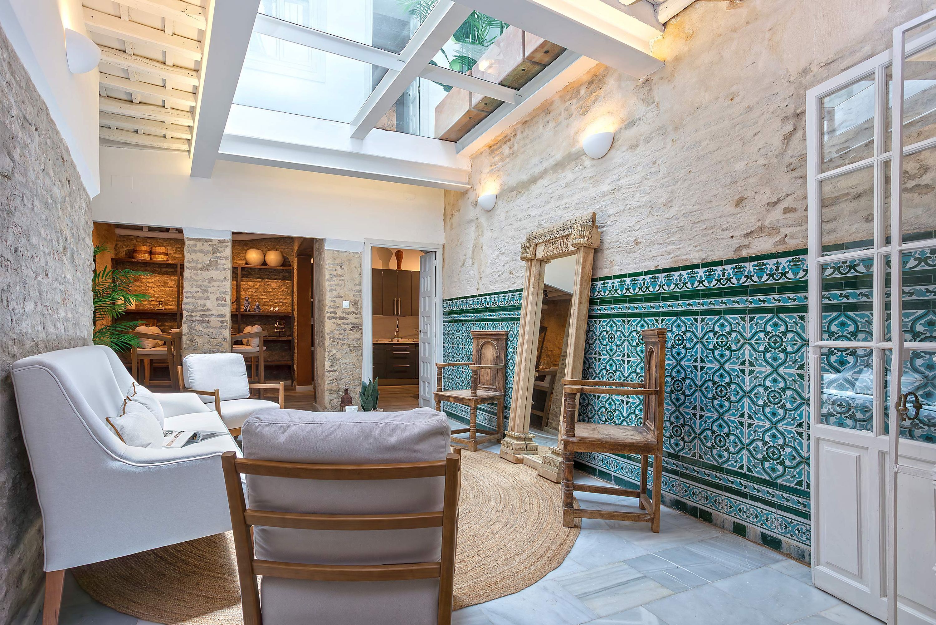 A spacious room with a high ceiling, a skylight, a seating area with chairs, a wooden chair, a woven rug, and a patterned wall.