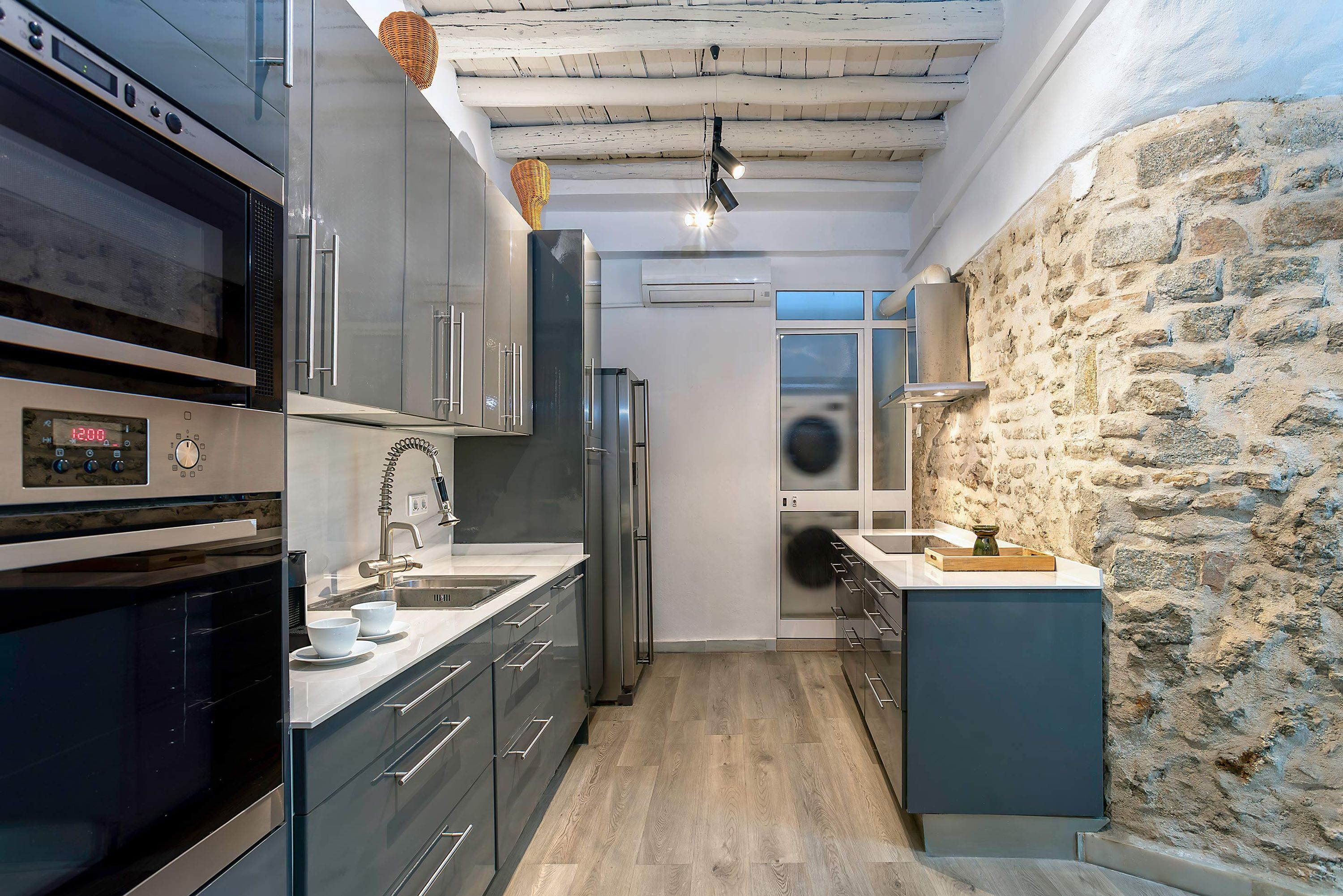 A modern kitchen with built-in appliances, a stone wall, and a wooden ceiling.