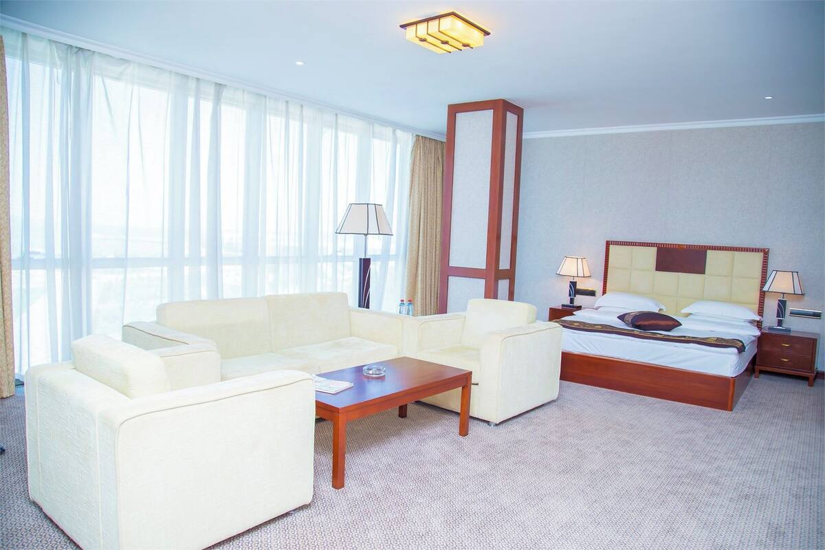 Una habitación de hotel con una cama, dos sillones, una mesa de centro, un escritorio y una lámpara.