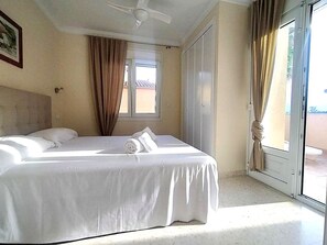 A hotel room with a bed, a ceiling fan, a window with curtains, and a view of the outside. - Ad1600 in Oliva With 3 Bedrooms and 2 Bathrooms (Oliva)