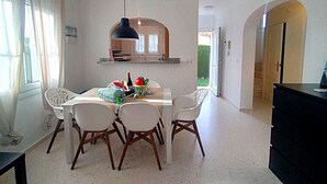 A dining area with a white table and chairs, a hanging light fixture, and a kitchen visible through an archway. - Ad1600 in Oliva With 3 Bedrooms and 2 Bathrooms (Oliva)