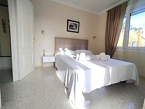 A hotel room with a bed, bedside tables, a nightstand, a framed picture on the wall, and a window with curtains. - Ad1600 in Oliva With 3 Bedrooms and 2 Bathrooms (Oliva)
