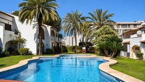 A swimming pool surrounded by palm trees and white buildings with arched windows. - Ap1122 in Denia With 1 Bedrooms and 1 Bathrooms (Denia)