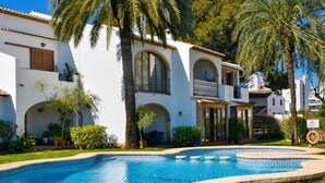 A pool surrounded by a white building with arched windows and balconies, palm trees, and a clear blue sky. - Ap1122 in Denia With 1 Bedrooms and 1 Bathrooms (Denia)