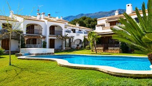A pool surrounded by white buildings with balconies, a clear blue sky, and mountains in the background. - Ap1122 in Denia With 1 Bedrooms and 1 Bathrooms (Denia)