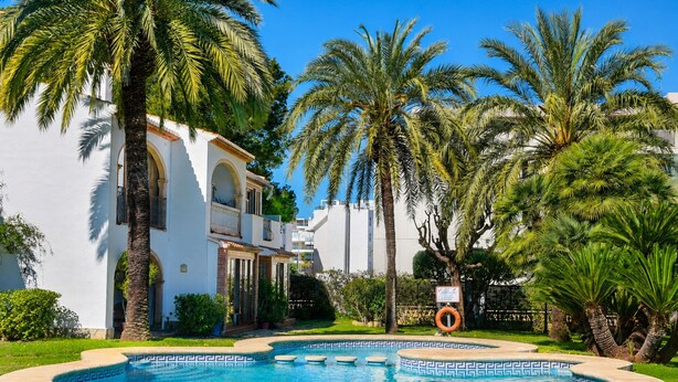 A swimming pool with a geometric tile pattern, surrounded by palm trees and a white building with arches. - Ap1122 in Denia With 1 Bedrooms and 1 Bathrooms (Denia)
