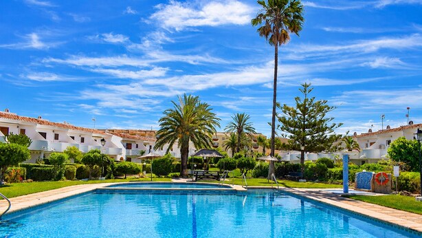 A swimming pool with clear blue water, surrounded by palm trees and a white building with red-tiled roofs. - Ad3223 in Denia With 3 Bedrooms and 1 Bathrooms (Denia)