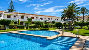 A swimming pool with a tiled deck, surrounded by a well-maintained garden and a white building with red-tiled roofs. - Ad3223 in Denia With 3 Bedrooms and 1 Bathrooms (Denia)