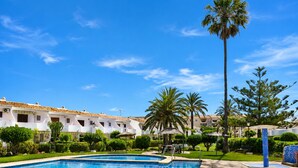 A swimming pool with a clear blue sky, surrounded by greenery and palm trees, with buildings in the background. - Ad3223 in Denia With 3 Bedrooms and 1 Bathrooms (Denia)