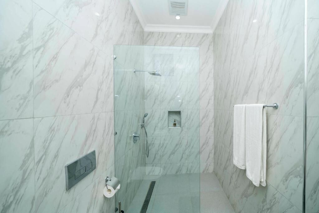 A modern bathroom with a glass-enclosed shower, marble walls, a towel rack, and a control panel.