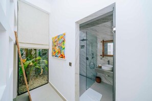 A bathroom with a glass shower enclosure, a white sink, and a colorful abstract painting on the wall. - Ô TALIA Hôtel and SPA (Nungwi)