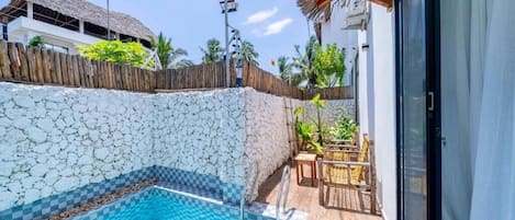 A swimming pool with a stone wall, a wooden fence, and a thatched-roof structure in the background.